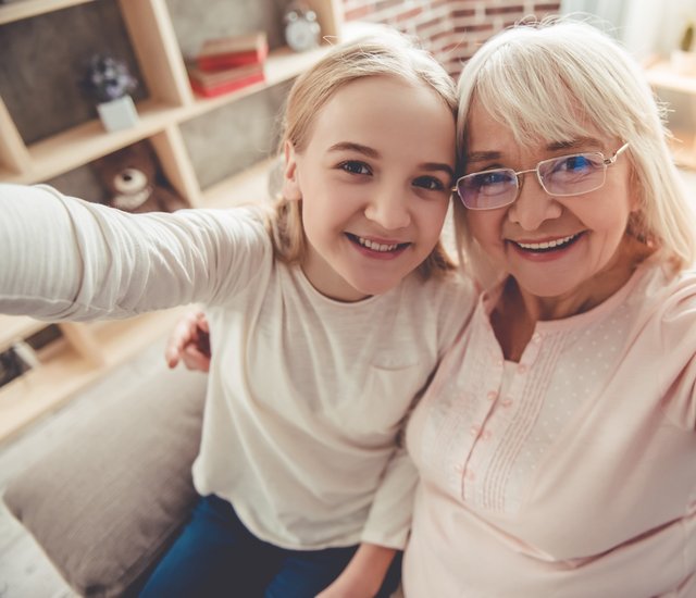 Eine junge Frau sitzt mit ihrer Oma auf der Couch. Sie machen gemeinsam ein Selfie.