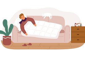 Ein Mann liegt zugedeckt auf einer Couch. Er trägt einen Schal um den Hals und einen dicken Pullover. Neben ihm liegt ein Thermometer. Auf der Couch schläft eine Katze.