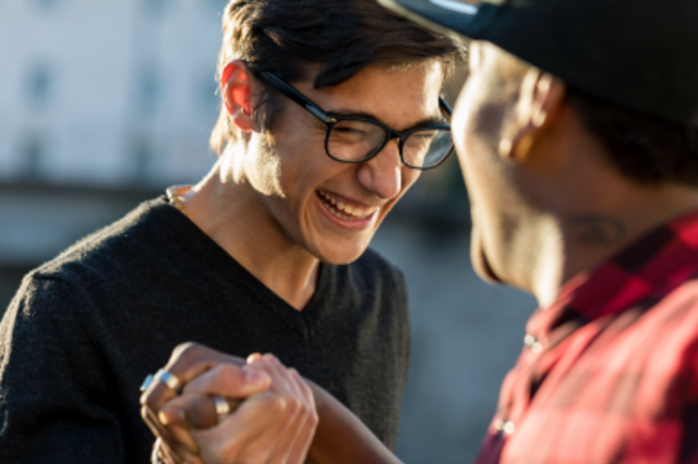 Zwei junge Männer geben sich einen Handschlag. Der Junge im Fokus trägt eine Brille und lacht.