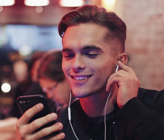 Ein junger Mann hat Kopfhörer in den Ohren und schaut auf sein Handy.