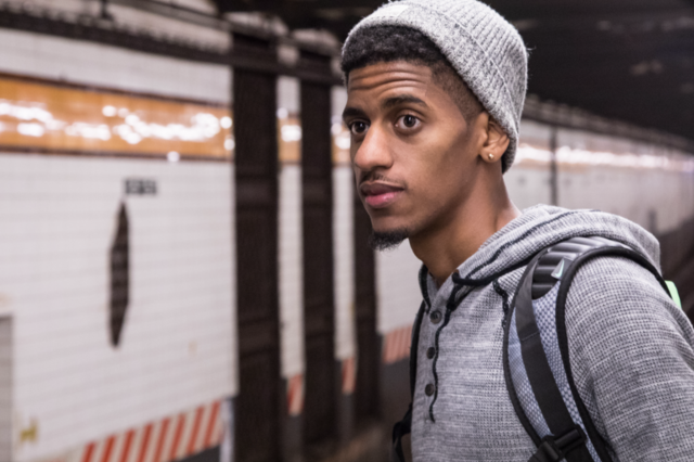 Ein junger Mann steht in einer U-Bahn Station und blickt in die Ferne.